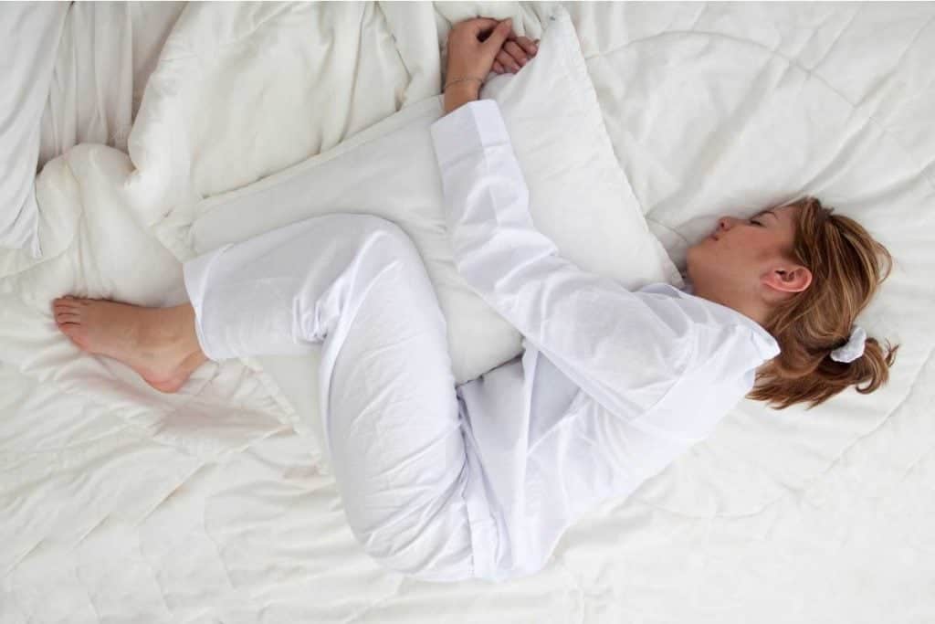 Woman hugging a pillow with knees while side sleeping