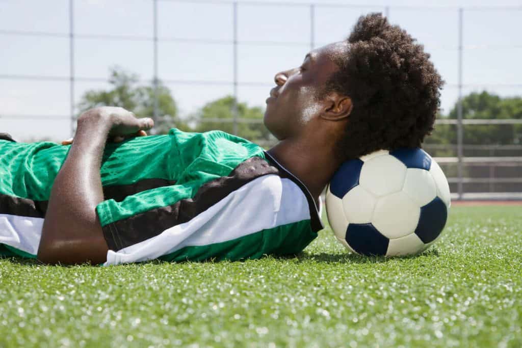 Soccer player lying down on a field on his ball