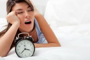 woman yawning in bed with alarm clock due to sleeping poorly at night