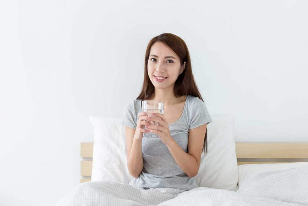 Woman smiling in bed and drinking water