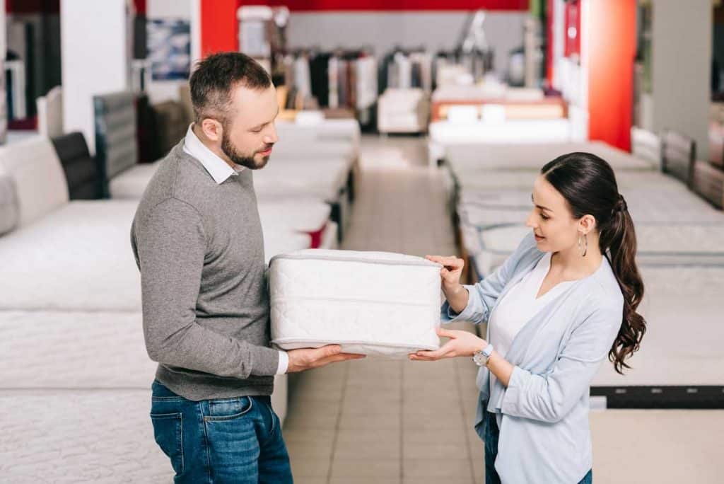 couple buying mattress on store and testing between firm and soft mattresses