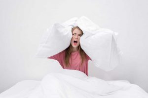 woman in bed holding pillows to her ears