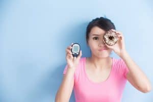 Woman-holding-a-donut-and-blood-sugar-meter