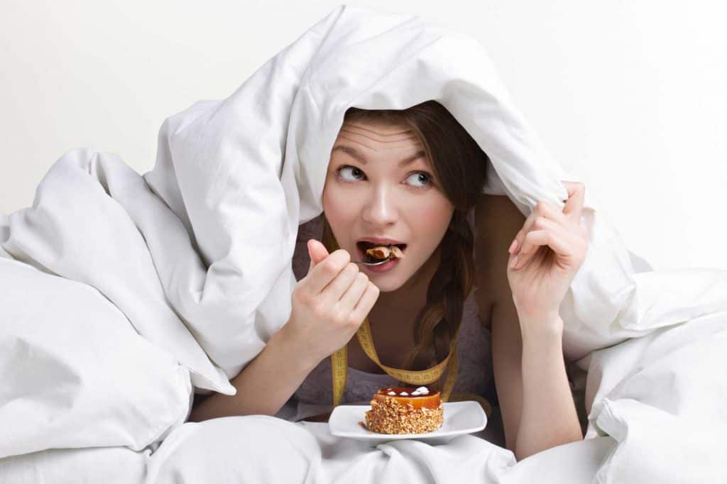 woman eating cake under bed covers